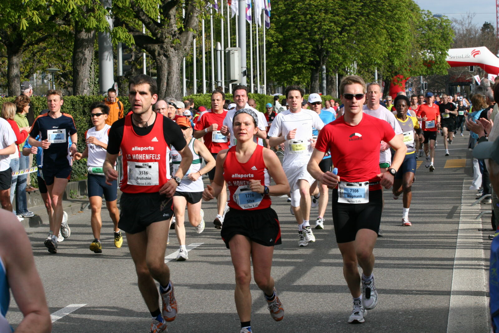Group of road-running participants wearing race numbers along a tree-lined street