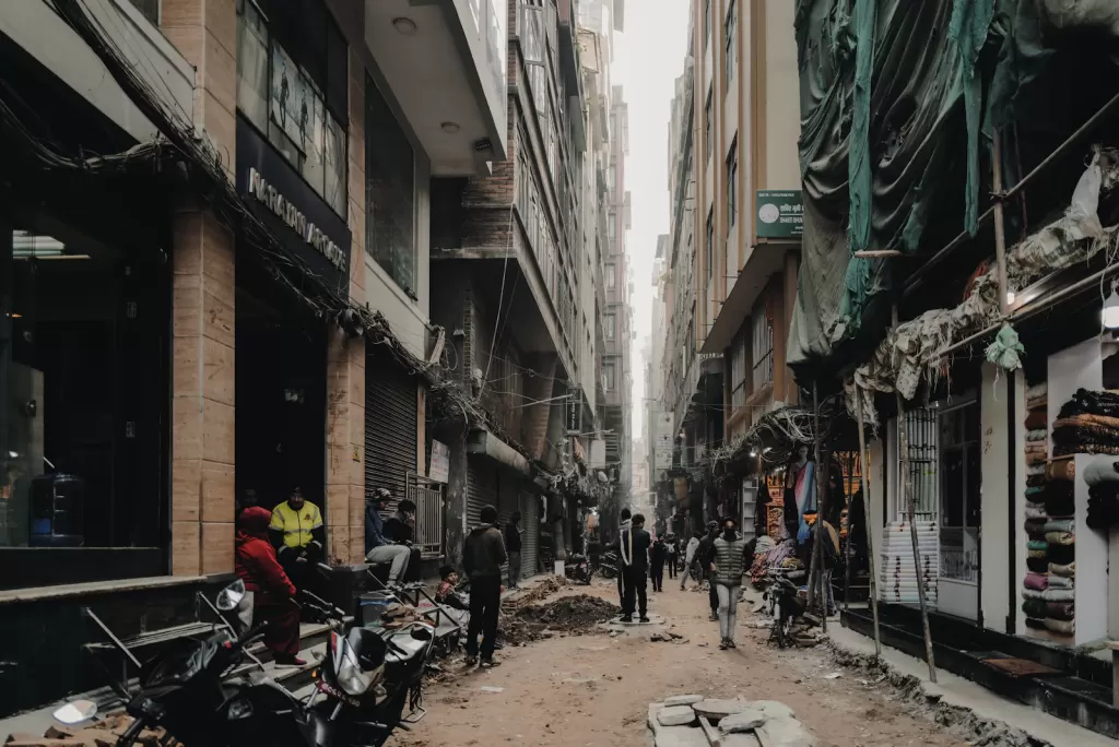 People walking along a Kathmandu street lined with shops and parked motorcycles