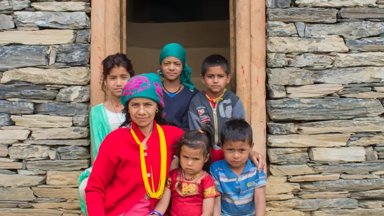 A family stands outside a stone home in Nepal, illustrating changing family and caregiving arrangements